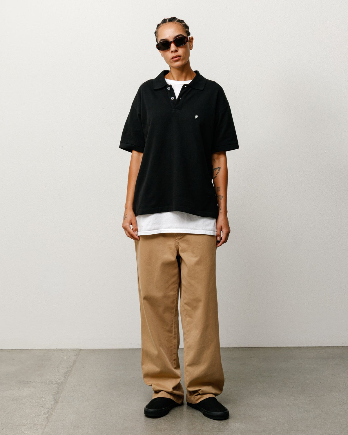 Stüssy Classic Pique Polo in Black, front model view over white tee, chest logo embroidery