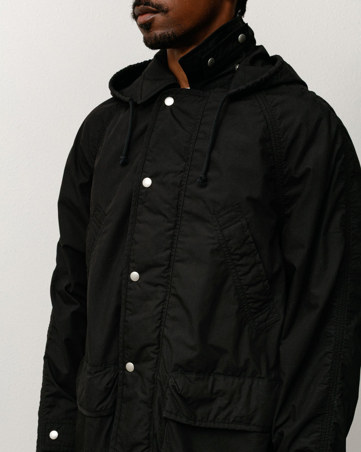 Lightweight field parka, unisex long-sleeve coat in black with snap placket and hood.
