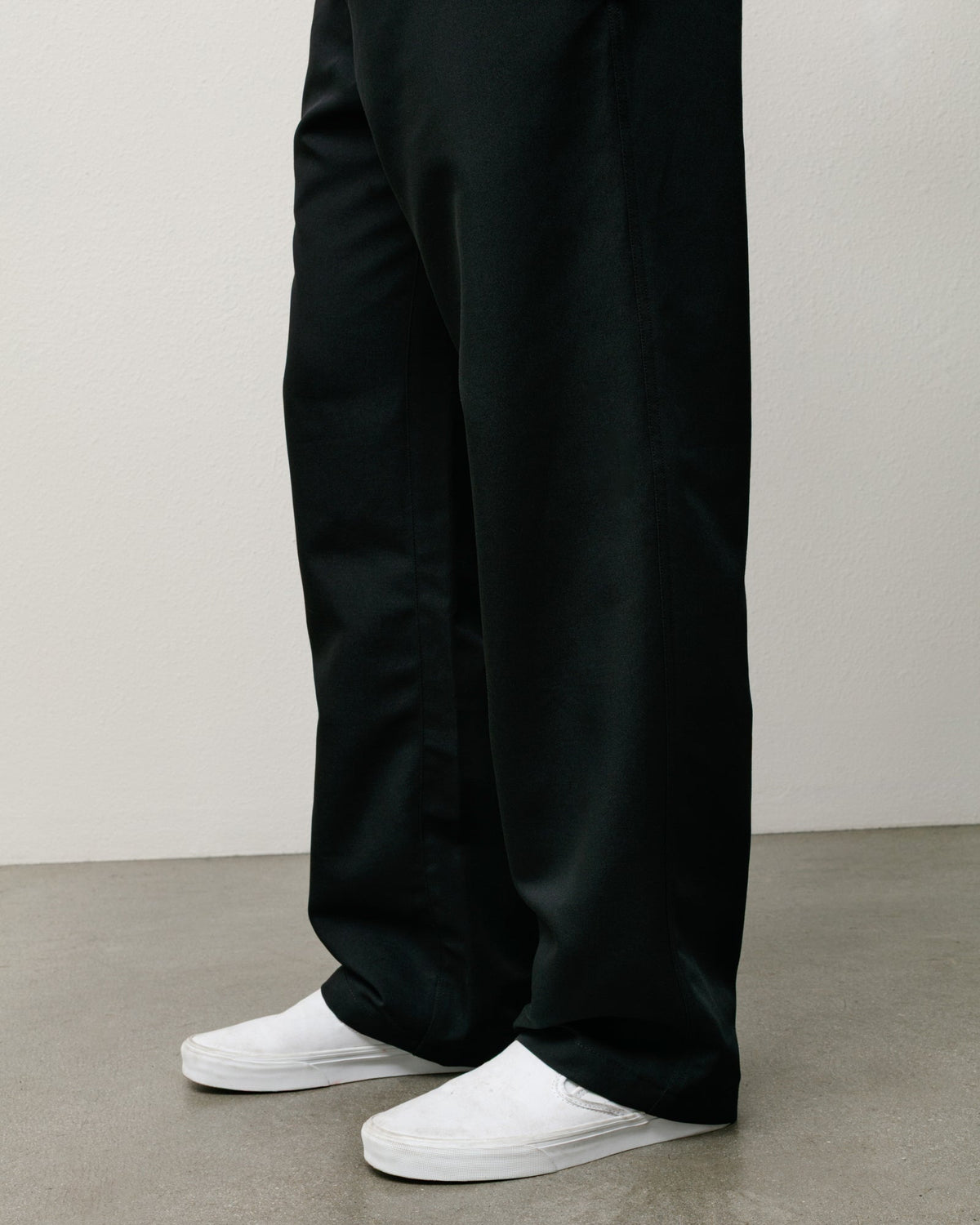 Stüssy Beach Pant in black, relaxed wide-leg twill, shown with white slip-on sneakers.