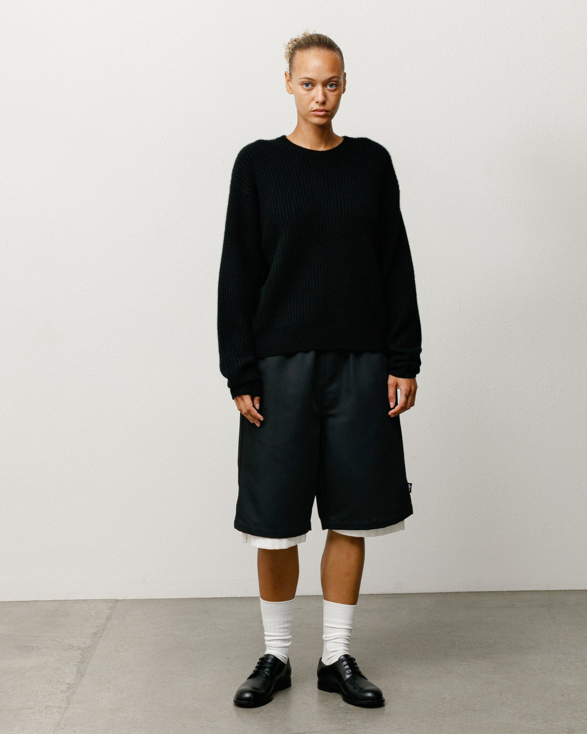 Person wearing a black sweater and black shorts against a plain background